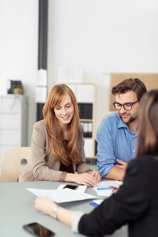 Young couple sitting in a meeting with an agent looking at a document together that she is presenting to them, view over the agents shoulder